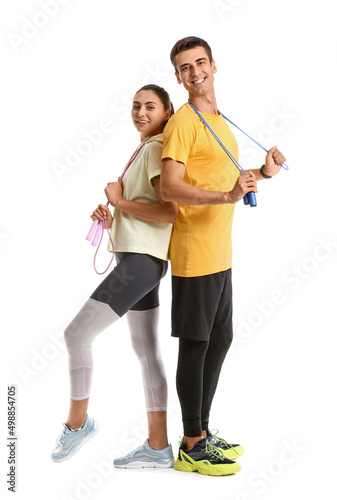 Sporty young couple with jumping ropes on white background