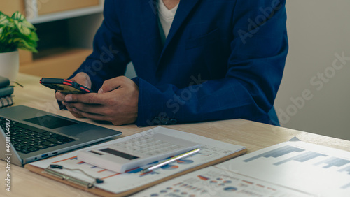 Businessman hand holding a smartphone, working on project statistics on devices. Presentation with graphs and an entrepreneur's accountant laptop analyzes financial data. show changes in the market