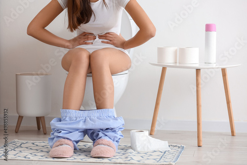 Photos Young woman suffering from bellyache on toilet bowl in restroom