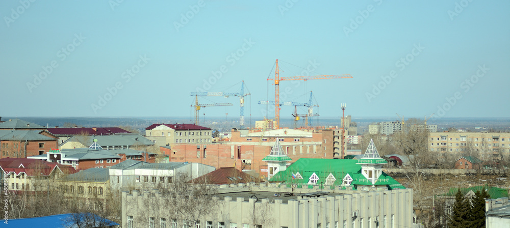 Panoramic shot of house roofs and construction cranes in the background.