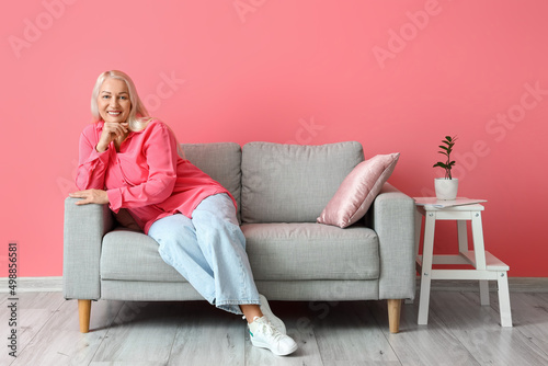 Mature woman sitting on sofa near pink wall