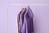 Rack with knitted sweaters on lilac background