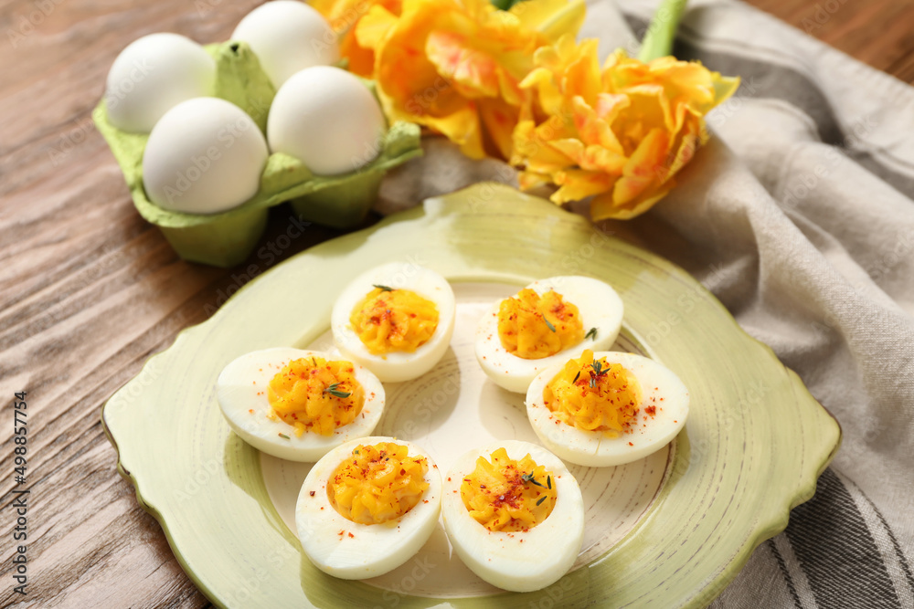 Plate with stuffed eggs, flowers and napkin on wooden background. Easter celebration Plate with stuffed eggs, flowers and napkin on wooden background. Easter celebration