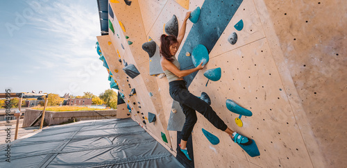 Bouldering climbing athlete woman training strength at outdoor gym boulder climb wall. Asian fit girl going up having fun in extreme sport hobby. Banner panoramic photo