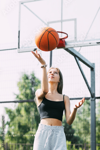A beautiful teenage girl throws a basketball up during a workout on a sports field or a school stadium © Sviatlana
