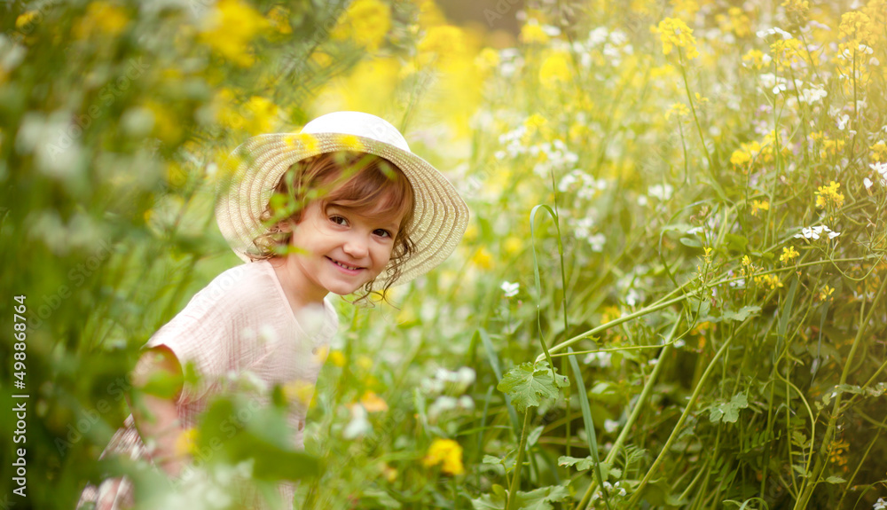 a babygirl in a hat in a rapeseed field is peeking out from behind the flowers a babygirl in a hat in a rapeseed field is peeking out from behind the flowers