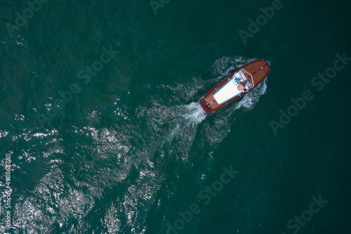 Classic wooden boat in motion drone view. People on an Italian wooden boat, top view. Old boat on Lake, Italy.