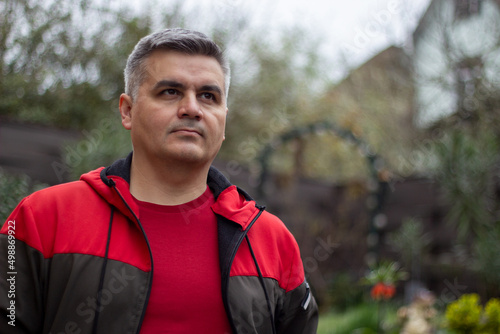 Portrait of a man 40-50 years old, gray-haired, swarthy. Looking at the camera. Big eyebrows. Red jacket. Trees on background