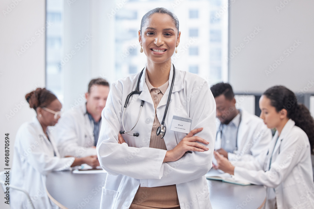 Confident with an awesome team behind me. Cropped portrait of an attractive young female doctor standing in the boardroom with her arms folded with her colleagues in the background. Confident with an awesome team behind me. Cropped portrait of an attractive young female doctor standing in the boardroom with her arms folded with her colleagues in the background.