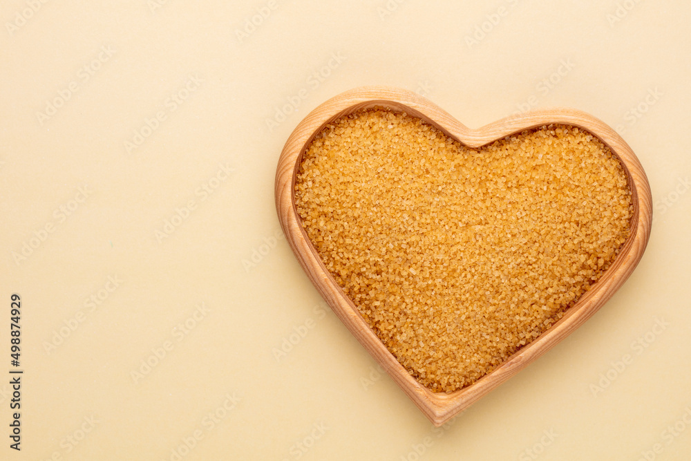 Brown sugar in heart wooden bowl shape on pasttel background.