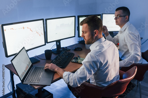 Analizing graphs together. Two stock traders working in the office with exchange technology