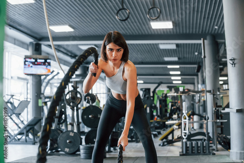 With special equipment. Woman in sportive clothes with slim body type is in the gym