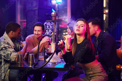 Woman smoking hookah. Group of friends having fun in the night club together