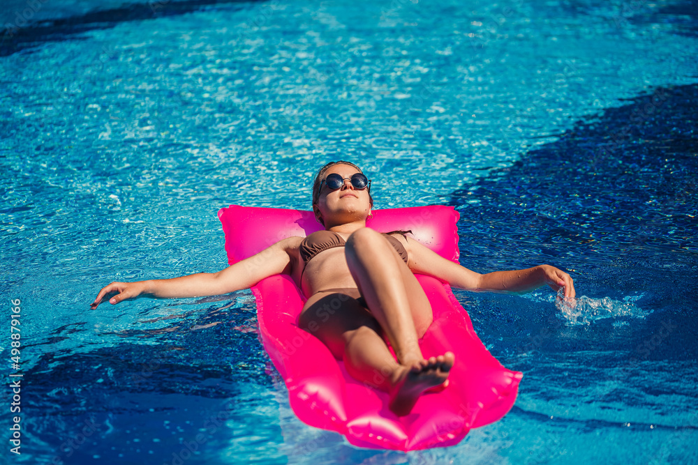 Sexy woman in a swimsuit lies on a pink inflatable mattress in the pool. Relax by the pool on a hot summer sunny day. Vacation concept