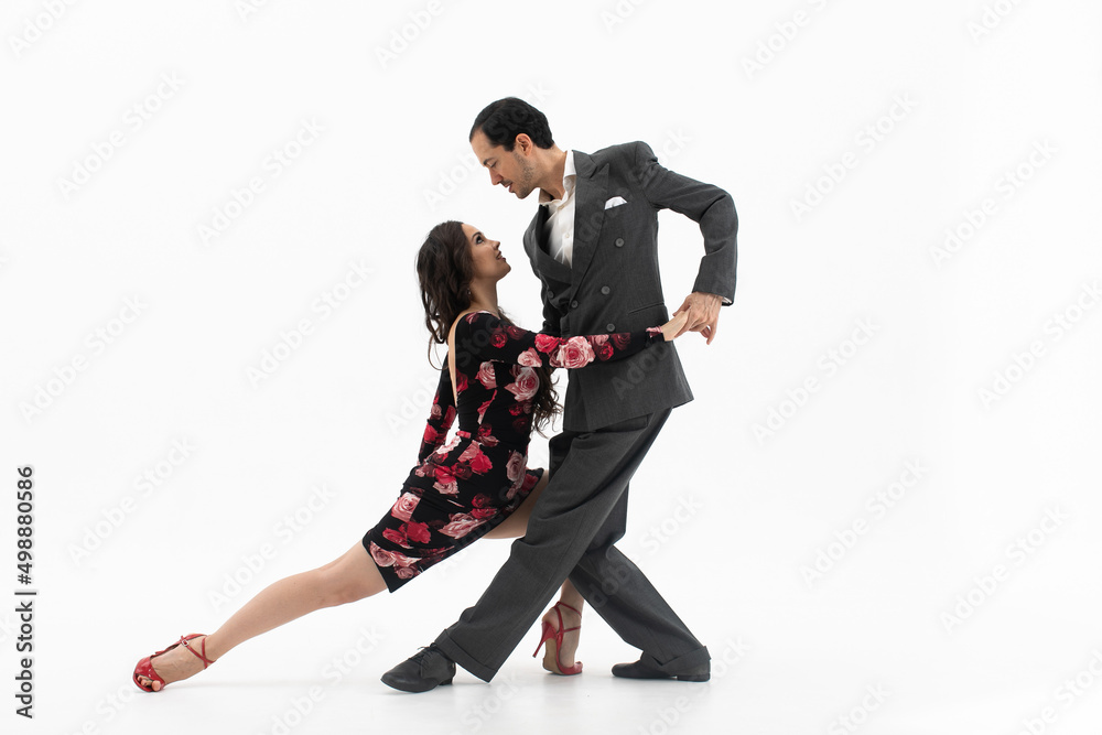 Couple of professional tango dancers in elegant suit and flowery print dress pose in a dancing movement on white background. Handsome man and woman dance looking eye to eye. - obrazy, fototapety, plakaty 