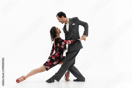 Couple of professional tango dancers in elegant suit and flowery print dress pose in a dancing movement on white background. Handsome man and woman dance looking eye to eye.