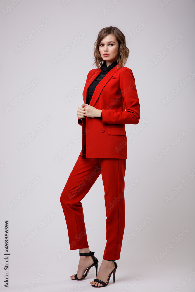 High fashion photo of a beautiful elegant young woman in a pretty red suit,  jacket, pants, trousers, black blouse posing on white background. Slim  figure, hairstyle, studio shot Stock Photo