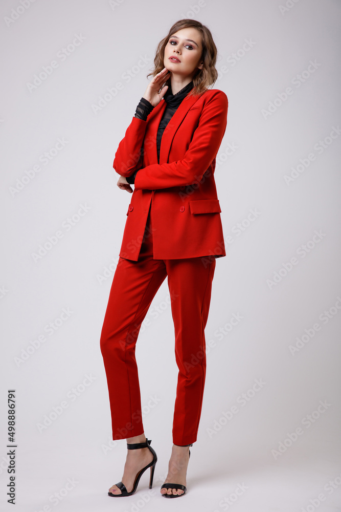 High fashion photo of a beautiful elegant young woman in a pretty red suit, jacket, pants, trousers, black blouse posing on white background. Slim figure, hairstyle, studio shot High fashion photo of a beautiful elegant young woman in a pretty red suit, jacket, pants, trousers, black blouse posing on white background. Slim figure, hairstyle, studio shot