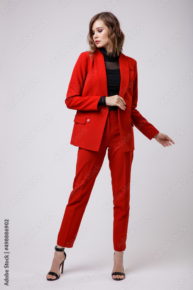 High fashion photo of a beautiful elegant young woman in a pretty red suit, jacket, pants, trousers, black blouse posing on white background. Slim figure, hairstyle, studio shot High fashion photo of a beautiful elegant young woman in a pretty red suit, jacket, pants, trousers, black blouse posing on white background. Slim figure, hairstyle, studio shot