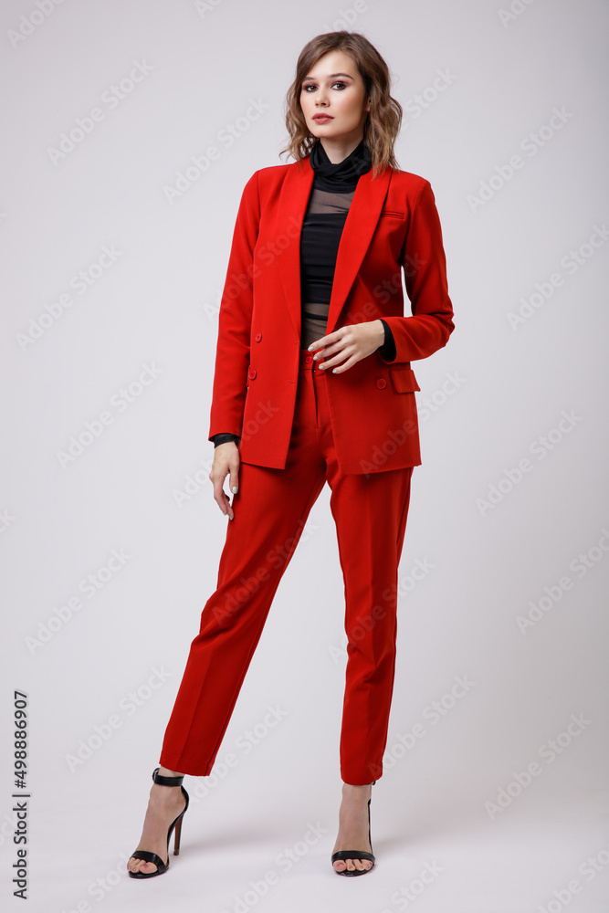 High fashion photo of a beautiful elegant young woman in a pretty red suit, jacket, pants, trousers, black blouse posing on white background. Slim figure, hairstyle, studio shot High fashion photo of a beautiful elegant young woman in a pretty red suit, jacket, pants, trousers, black blouse posing on white background. Slim figure, hairstyle, studio shot