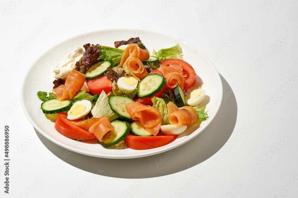 Salad with salmon, cucumber, tomatoes and cream cheese on a white plate on a white background