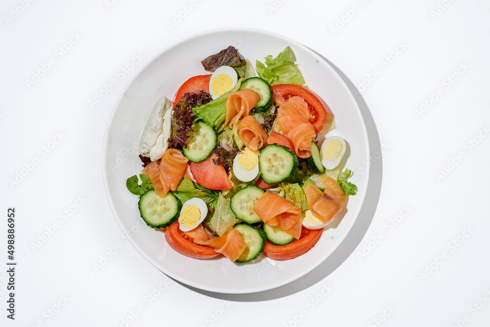 Salad with salmon, cucumber, tomatoes and cream cheese on a white plate on a white background