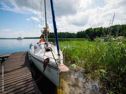 moored sailboat near old wooden pier on a lake shore in a sunny summer day