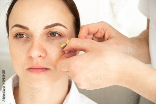 Close-up of cosmetologist making taping face procedure using yellow tapes. Anti-aging treatment against wrinkles.