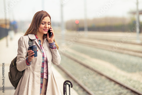 A beautiful woman in her 30s is using a mobile phone while waiting for a train at a train station. © DusanJelicic