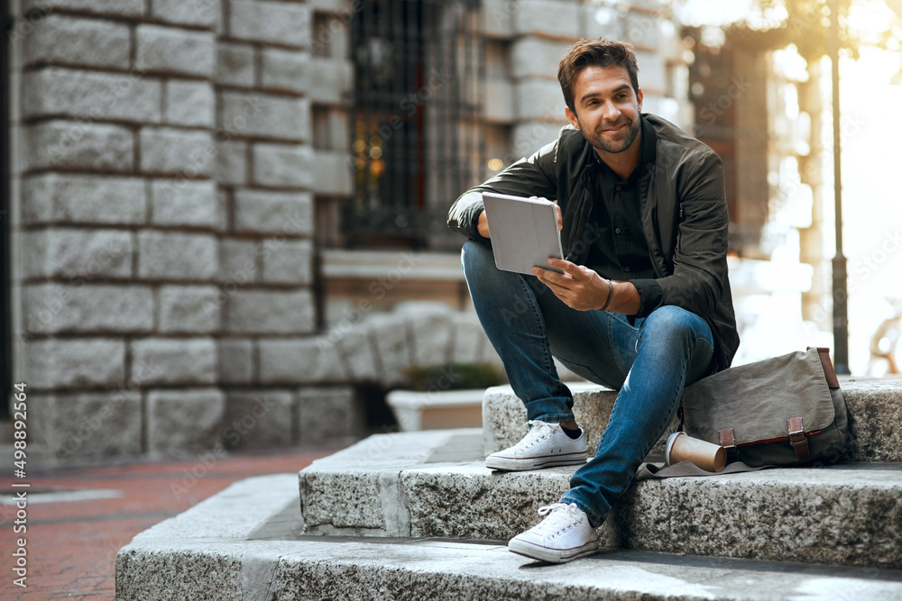 Obraz premium Some people were made for the city life. Full length shot of a handsome young man using his tablet while traveling through the city.