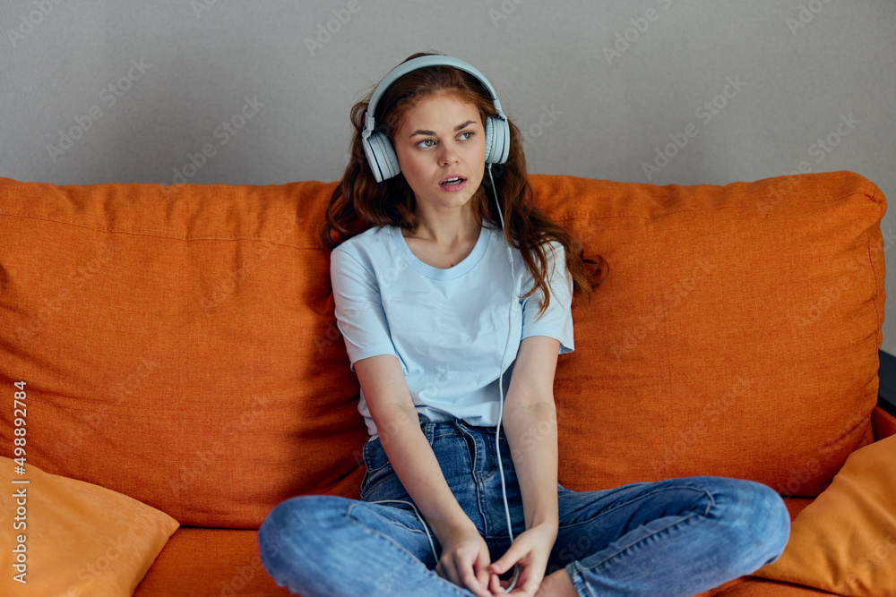 portrait of a woman on the orange sofa listening to music with headphones Lifestyle portrait of a woman on the orange sofa listening to music with headphones Lifestyle