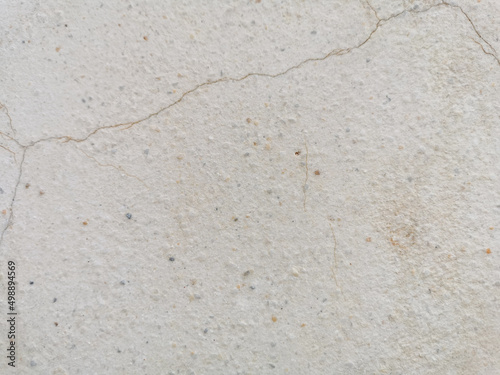 Old stucco wall with marble grains and rusty cracks. Beige cracked cement with fine gravel surface. Ferruginous cracks on plaster wall.