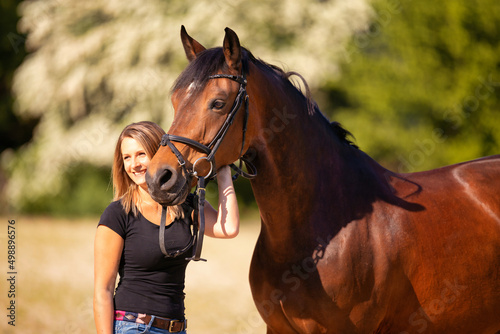 Horse with partial body with young woman against blurred background in sunshine..