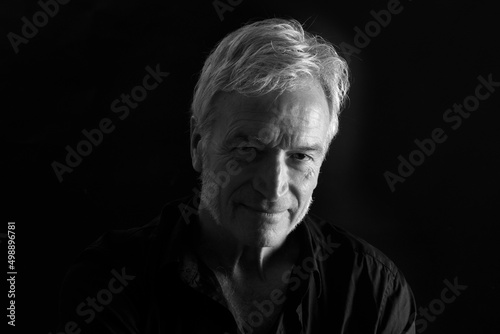 front view of low key portrait of a senior man looking at camera on black background © curto