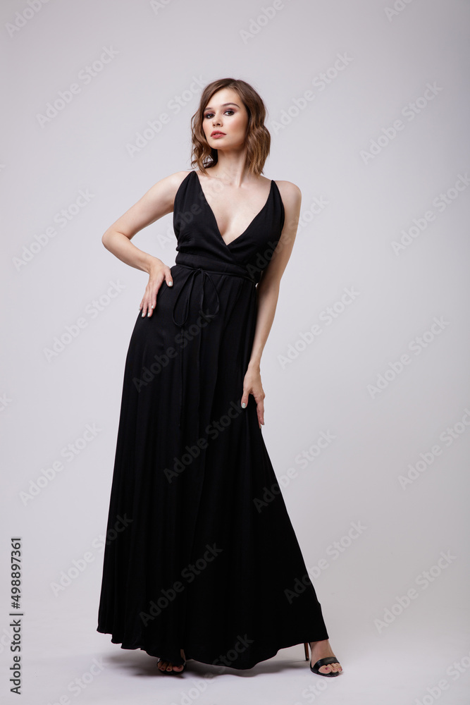 High fashion photo of a beautiful elegant young woman in a pretty black evening party dress with a deep neckline posing on white background. Slim figure, hairstyle, studio shot. High fashion photo of a beautiful elegant young woman in a pretty black evening party dress with a deep neckline posing on white background. Slim figure, hairstyle, studio shot.