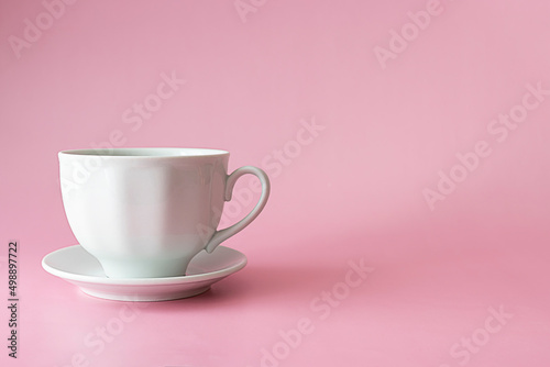 A ceramic white cup on a small saucer on a pink table. Light pink background, text space