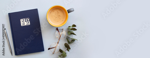 Colored diary for the year 2022, pen, glasses and coffee latte on gray background. New year planning concept. Minimalistic workstation. Copy space. photo