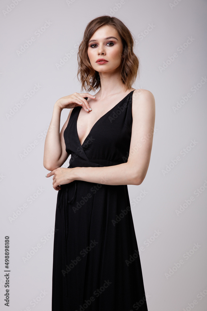 High fashion photo of a beautiful elegant young woman in a pretty black evening party dress with a deep neckline posing on white background. Slim figure, hairstyle, studio shot. High fashion photo of a beautiful elegant young woman in a pretty black evening party dress with a deep neckline posing on white background. Slim figure, hairstyle, studio shot.