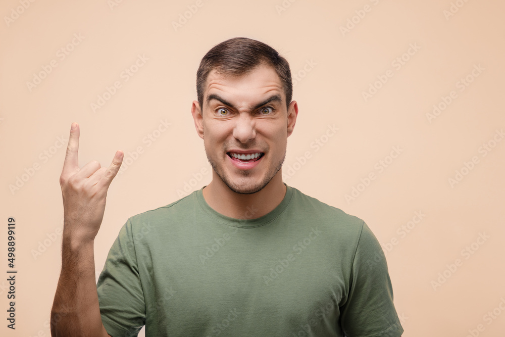 portrait of contented man with short hair shows goat gesture, horns on beige background portrait of contented man with short hair shows goat gesture, horns on beige background