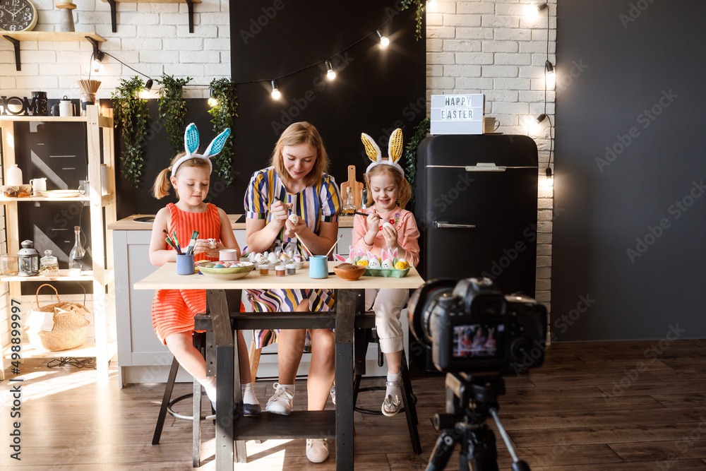 Naklejka premium Mom and her two daughters wearing bunny ears decorating Easter eggs, preparing for Easter holiday.