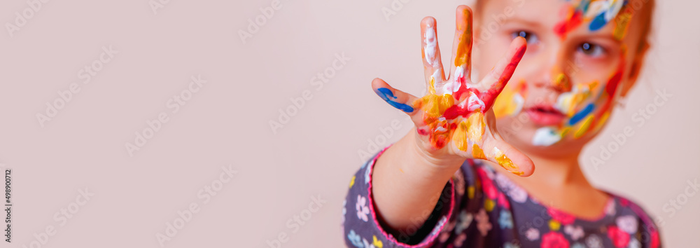 Hands and face of cute young girl painted in colorful paints. Children's makeup. Copy space.
