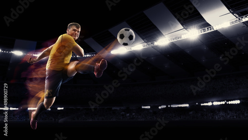 Professional football or soccer player in action on stadium with flashlights  kicking ball for winning goal. Concept of sport  competition  motion  overcoming.