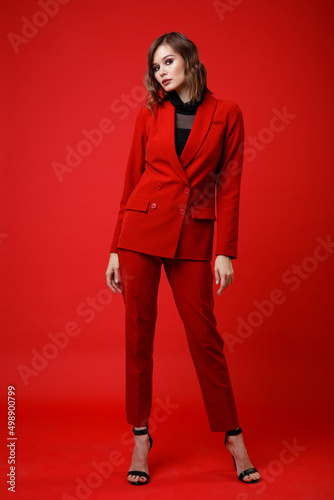 High fashion photo of a beautiful elegant young woman in a pretty red suit, jacket, pants, trousers, black blouse posing on background. Slim figure, hairstyle, studio shot. Monochrome, total red