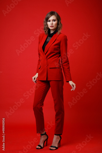 High fashion photo of a beautiful elegant young woman in a pretty red suit, jacket, pants, trousers, black blouse posing on background. Slim figure, hairstyle, studio shot. Monochrome, total red
