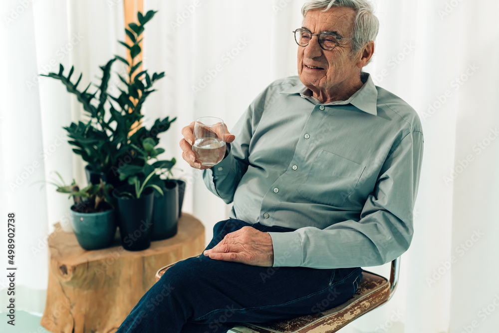 elderly man sitting on the chair holding a glass of water - old man hydrating himself elderly man sitting on the chair holding a glass of water - old man hydrating himself