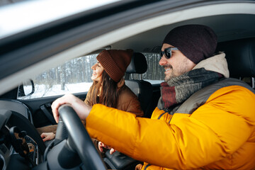 Family couple sitting in car in winter clothes iin snow forest