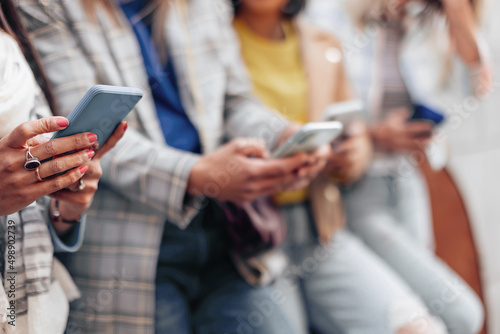 detail of the hands of an Indian woman typing on the mobile phone - people in background standing in line with mobile phones