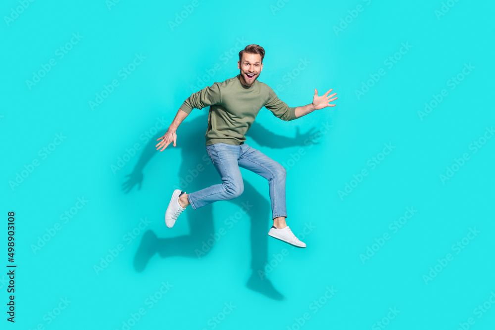 Full size photo of millennial blond guy jump wear sweater jeans sneakers isolated on turquoise background