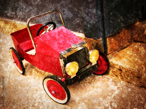 Childhood grungy dream. Red vintage toy car near entrance to the house. Retro old photo with scratches. photo