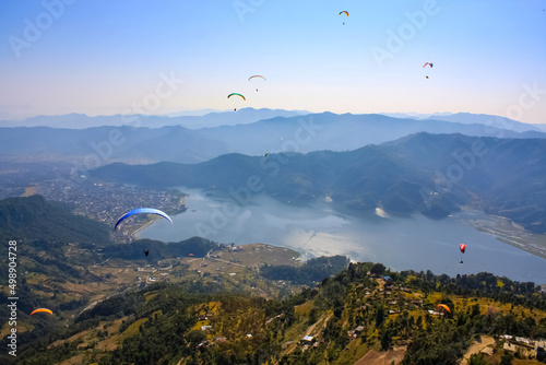 Colorful paraglades flight over Phewa lake and Pokhara. Scenic aerial landscape with lake, meadows, mountains and flying paraglades. Paraglading Himalayan mountains and lake.